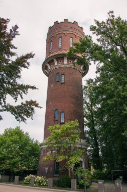 Uzun yeşil ağaçlı lüks bir bahçede antik bir su kulesinin dikey görüntüsü.