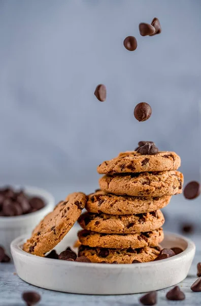 The chocolate chips in the air dropping on a stack of chocolate chip cookies on white plate