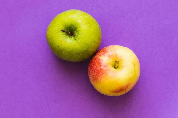 A flat ray of green apple and red apple on purple surface with copy space