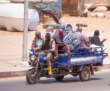 Bir üçlü, birçok insanı taşıyan bir caddede seyahat eder. Şehir Nouakchott, Moritanya 'dır..
