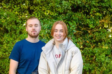 Beyaz tenli genç bir çiftin parkta kameraya baktığı sığ bir odak noktası.