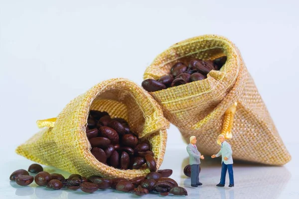 Çuval dolusu kavrulmuş kahve çekirdekleri beyaz arka planda, tüccarlar önünde duruyor, makro fotoğraf.