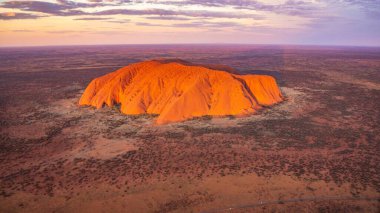 An aerial shot of Uluru Rock in Australia during sunset on desert land with purple sky clipart