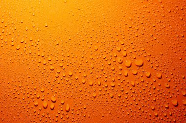 Turuncu bir yüzeydeki su damlalarının yakın plan çekimi.