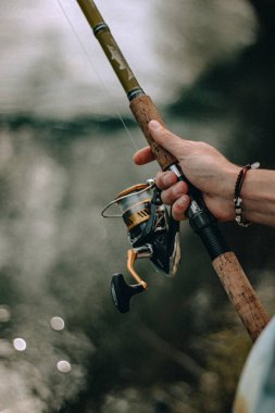 Bulanık bir arkaplanda olta tutan bir elin dikey ve yüzeysel odak noktası.