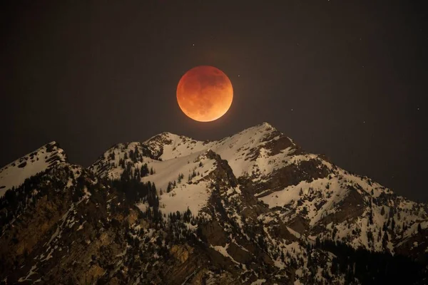 Оранжевая Полная Луна Светит Ярко Над Заснеженной Скалистой Горой Ночью — стоковое фото