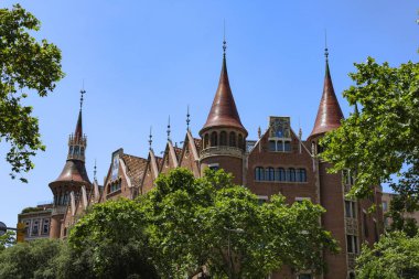 İspanya, Barcelona 'da mavi gökyüzünün altındaki bazı ağaçların arkasındaki tipik bir ortaçağ İspanyol kalesinin yatay görüntüsü