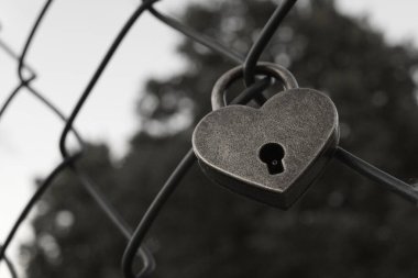 Siyah ve beyaz tel örgülere kilitlenmiş kalp şeklinde bir kilit.