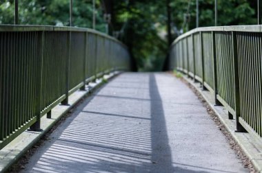 Güneş ışığının altında metal parmaklıkları olan bir yaya köprüsü.