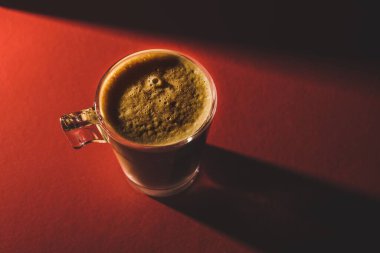Kırmızı bir masanın üstünde köpüklü kahve bardağının üst görüntüsü.