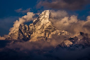Ama Dablam 'ın zirvesi bulutlar ve sisle kaplı güneş ışığını yansıtıyor.