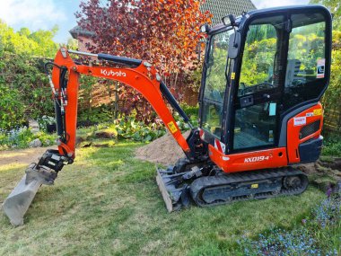 Yeşil bir bahçede küçük kırmızı bir Kubota kazıcısı.