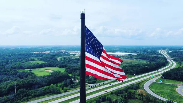 A closeup of waving American flag against the background of nature and highway under cloudy sky