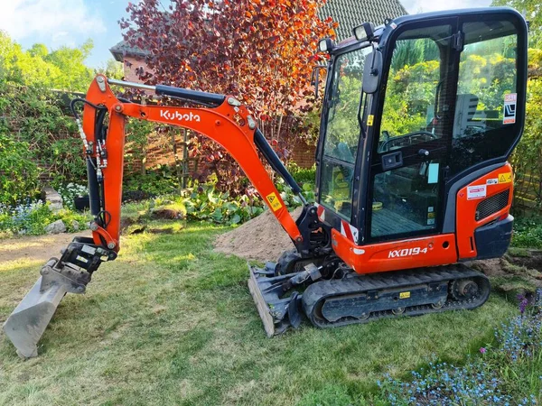 Yeşil bir bahçede küçük kırmızı bir Kubota kazıcısı.