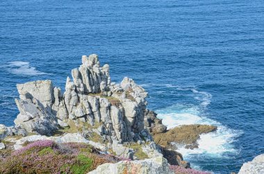 Gün ışığında suyla çevrili kayalık bir plaj manzarası.