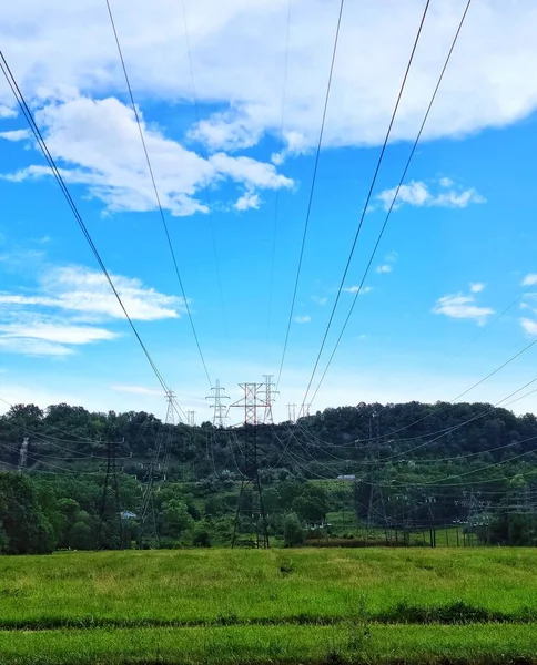 Vertikální Záběr Elektrického Vedení Zeleném Poli Proti Zatažené Modré Obloze — Stock fotografie