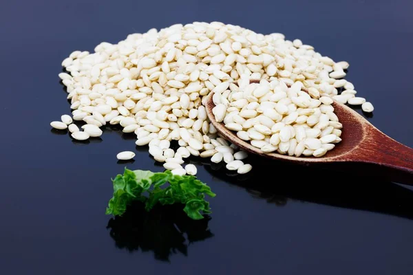 A closeup of short-grain rice with a wooden spoon and green lettuce on a blue surface.