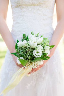 Elinde çiçek buketi tutan beyaz gelinlikli bir gelinin dikey yakın çekimi.