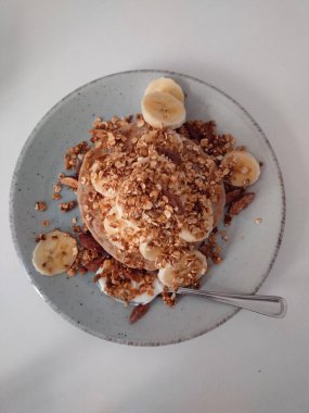 Gri bir tabakta dilimlenmiş muz ve yulaf ezmesi tohumları olan bir gözlemenin dikey görüntüsü.