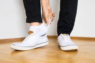 A closeup of a person putting on white sneakers with shoehorn clipart