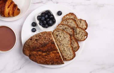 Beyaz bir masada servis edilen yaban mersinli ve kapuçinolu ekmeğin üst görüntüsü.