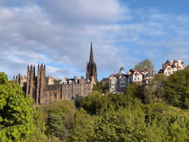 Edinburgh 'daki eski binalar yemyeşil ağaçların arkasında mavi bulutlu arka planda