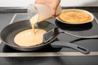 Bir erkek insan eli, aileye kahvaltı hazırlarken krep için hamuru kızartma tavasına doldurur.