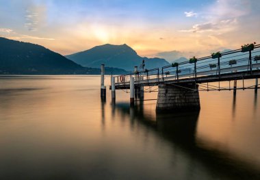 İtalya 'da gün batımında dağlara karşı gölde iki tahta direğin uzun pozu