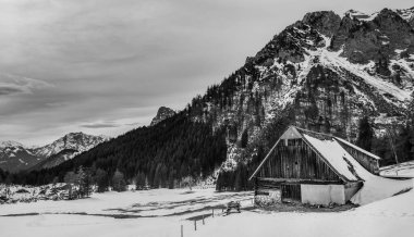 Gri renkli karlı dağlar ve ahşap bir ev.