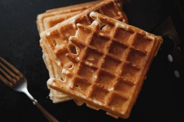 Siyah bir yüzeyde gümüş çatallı gevrek waffle 'ların üst görüntüsü.