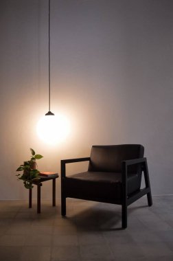 Modern küçük bir masa ve yuvarlak bir lambayla siyah deri bir koltuğun dikey çekimi..