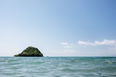 Ortasında çimen kaplı bir kaya olan bir deniz manzarası.