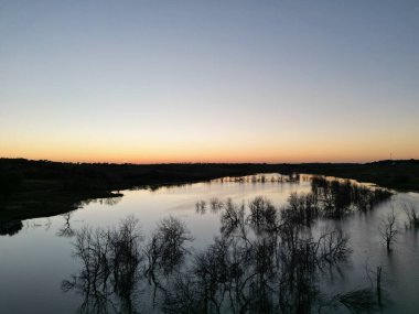 Bulutsuz gün batımında ayna gölünün yanındaki tepelerin silueti.