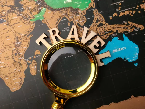 A flat lay with a magnifying glass and wooden TRAVEL on a world map background