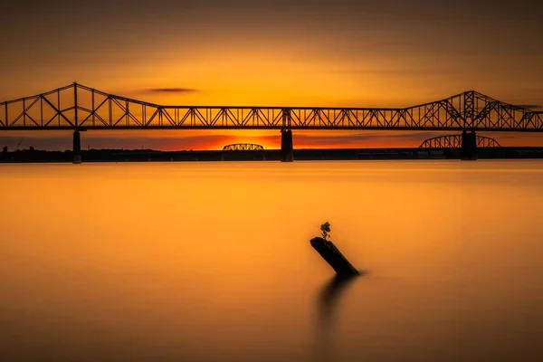 オハイオ川に架かる橋のシルエットオレンジの夕焼け空の下に木の切り株 — ストック写真