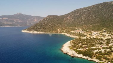 Mavi denize karşı yeşil çalılarla kaplı dağların kuş bakışı görüntüsü.