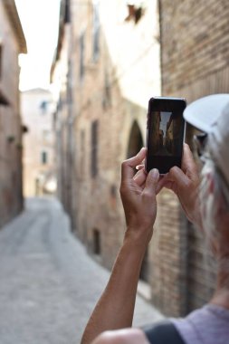 İtalya 'nın eski Amandola kasabasında fotoğraf çekmek için cep telefonu kullanan kadın turist.
