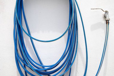 Su musluğuna bağlı beyaz bir duvarda asılı mavi bir hortum.