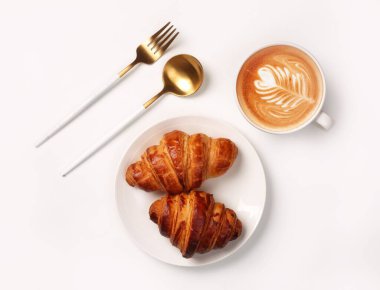 Beyaz bir masada servis edilen kruvasan ve kapuçino manzarası.