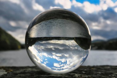 Su ve bulutlu gökyüzünün baş aşağı yansıttığı bir gölün yakınındaki büyük kristal küreye yakın çekim.