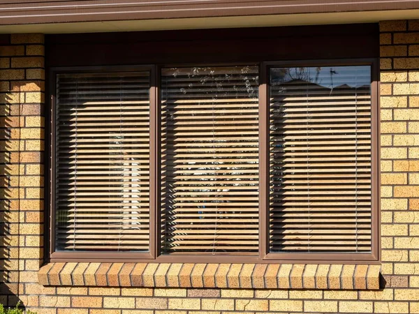 Aluminum frame window with wooden blinds. Bright amber brick wall with dark mortar.