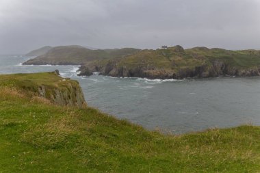 Çiçekli bir nehrin her iki yakasındaki yeşil tepeler ve kayalıklardan oluşan güzel bir manzara, İrlanda, Birleşik Krallık