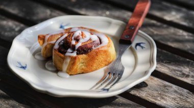 Ahşap bir yüzeydeki çatalın yanındaki tabakta taze pişmiş tarçın rulolarının yakın çekimi.