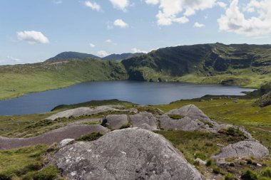 Yeşil ve kayalık tepelerin ortasındaki küçük bir gölün güzel doğal manzarası.