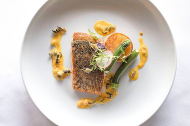 Yabani barramundi balıklı, rezene ve kabakla servis edilen bir tabağın yakın çekimi.