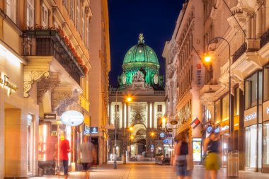 Viyana 'da aydınlık bir gece. İnsanlar aydınlık bir sokakta mağazaların önünden geçiyor.