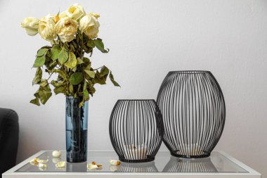 Düşen yapraklar ve siyah fener tutacaklarıyla yaşlanmış ve kurumuş beyaz güllerin yakın çekimi.