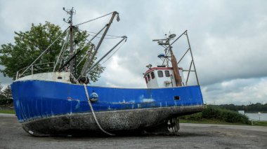 Almanya 'da Nord Ostsee Kanalı' nda arkasında ağaçlar olan terk edilmiş mavi bir balıkçı teknesi.