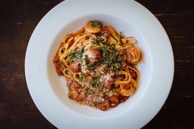 Mantarlı ve kırmızı soslu beyaz tabakta servis edilen bir spagetti.