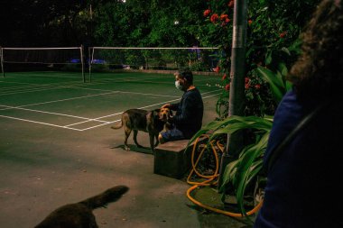 Tayvan 'ın Taipei şehrinde gece tenis kortunda köpekle oturan bir erkeğin görüntüsü.
